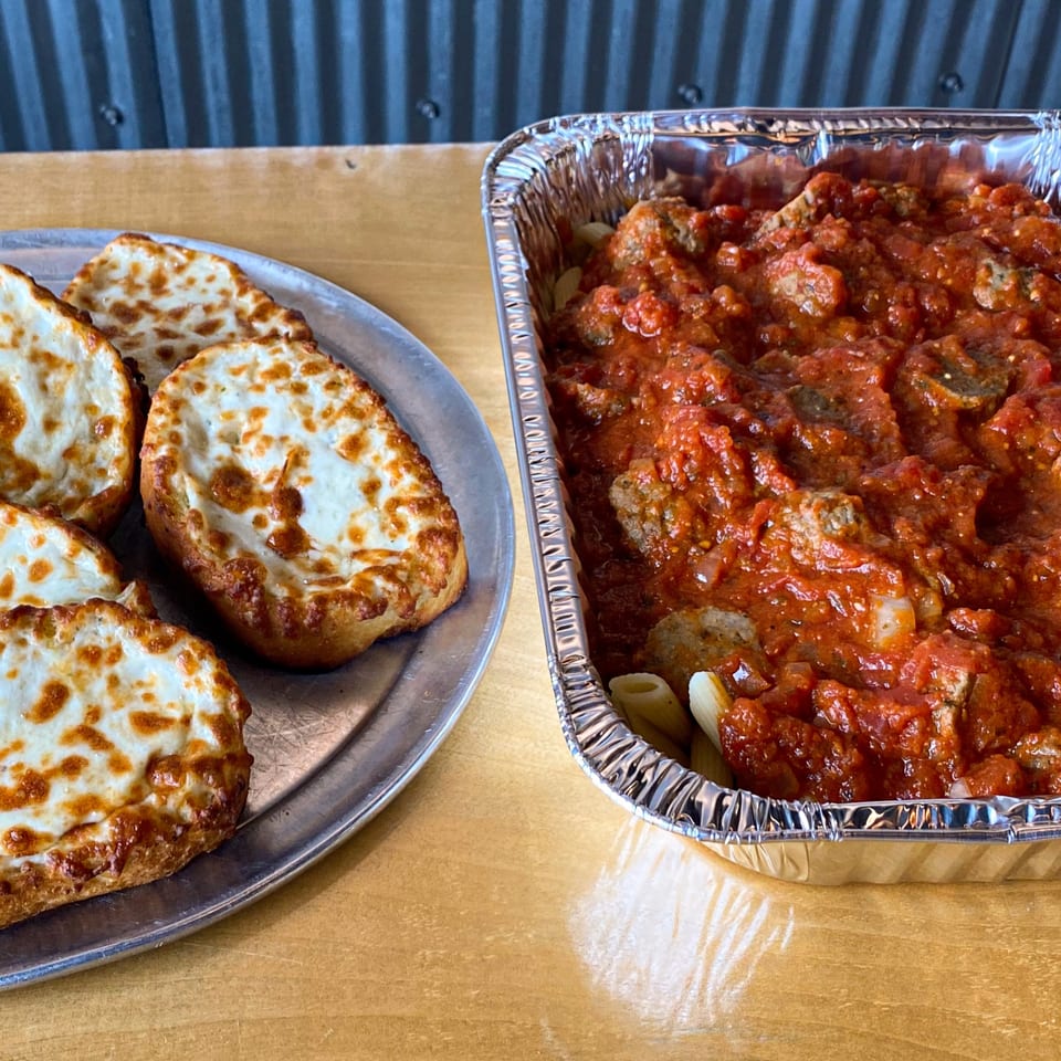 A foil pan of baked ziti with meatballs and a plate of cheesy garlic bread from Jimmy's Pizza.