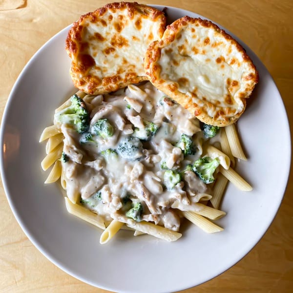Creamy penne pasta with chicken and broccoli, served with two pieces of cheesy garlic bread.