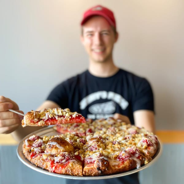 A smiling Jimmy's Pizza employee holding a dessert pizza with strawberry, crumble, and icing.