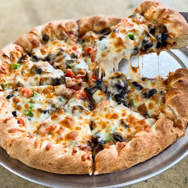 A slice of Jimmy's Pizza with melted cheese, black olives, and green peppers being lifted from the pie.