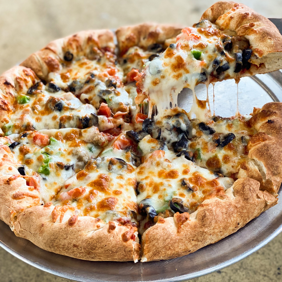 A slice of Jimmy's Pizza with melted cheese, black olives, and green peppers being lifted from the pie.