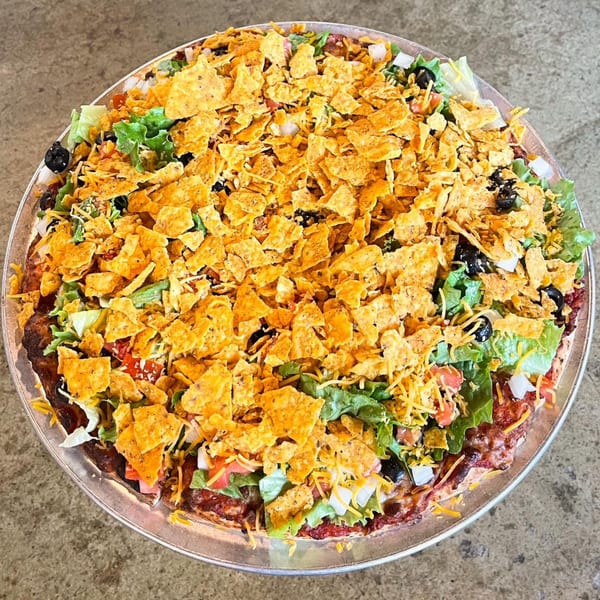A taco pizza from Jimmy's Pizza, topped with lettuce, tomatoes, black olives, cheese, and crushed tortilla chips.
