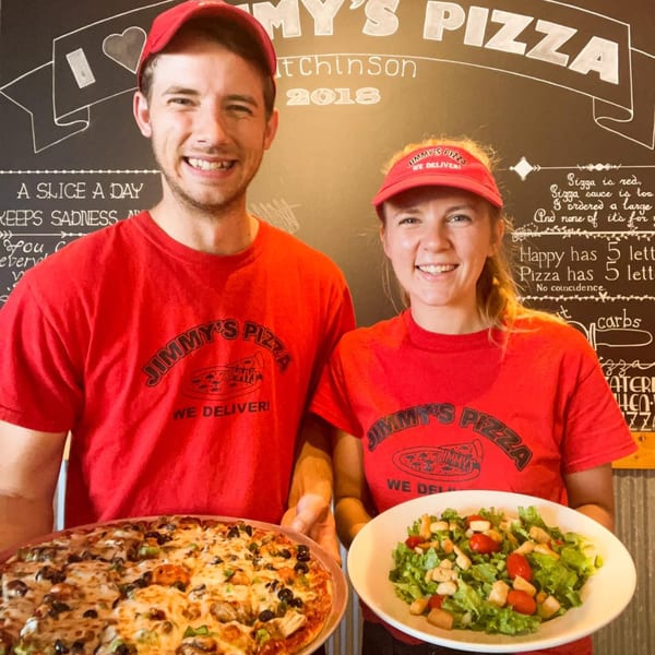 Two smiling Jimmy's Pizza employees in red shirts holding a pizza and a salad.