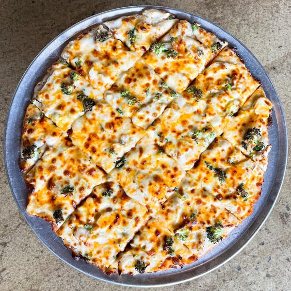 Top-down view of a Jimmy's Pizza broccoli and cheese pizza, cut into small squares on a metal pan.