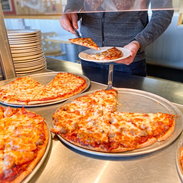 A person serving themselves a slice of cheese pizza from a buffet line at Jimmy's Pizza.