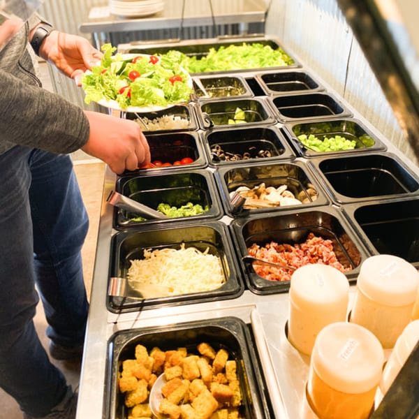 A person fills a plate with fresh salad and toppings from a salad bar at Jimmy's Pizza.