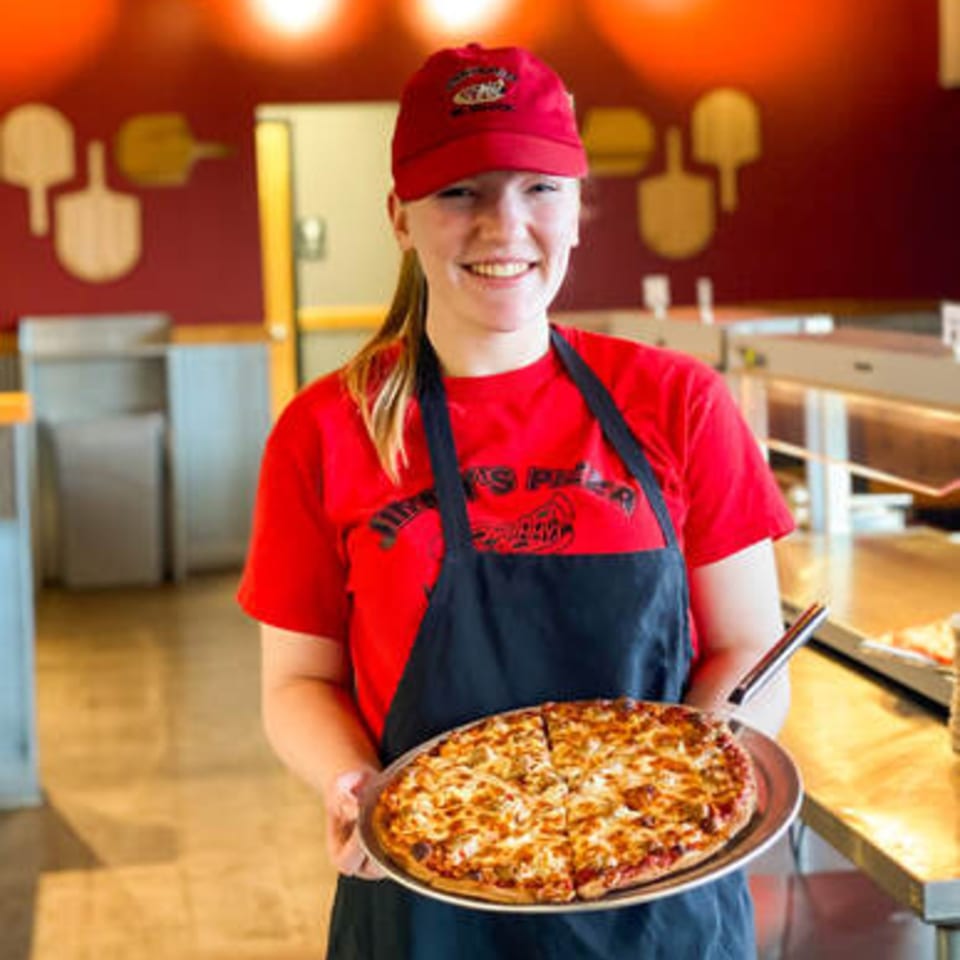 Smiling Jimmy's Pizza employee in red shirt and apron holding a freshly baked pizza.