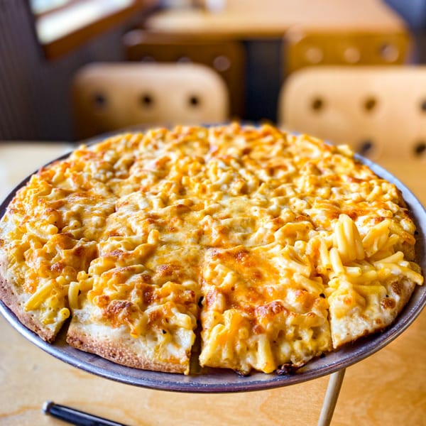 A whole mac and cheese pizza, sliced, on a metal stand in a restaurant setting.